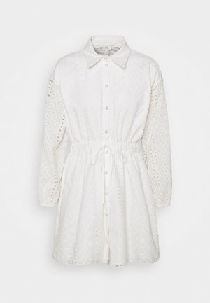 Witte, geborduurde shirtjurk met een kraag, lange mouwen en een ceintuur in de taille. De textuur van de stof heeft uitgesneden patronen en knopen aan de voorkant.