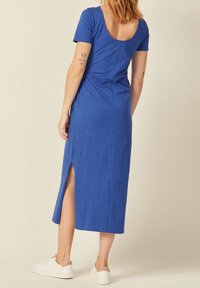 Vestido azul de manga corta, a la altura de la rodilla, con escote en la espalda, abertura lateral y textura suave. Combinado con zapatillas blancas.