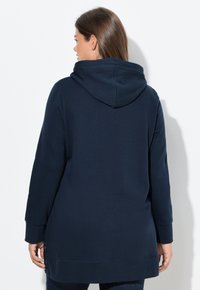 Felpa con cappuccio blu navy, maniche lunghe, spacchi laterali all'orlo e una consistenza morbida, mostrata di spalle.