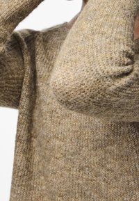 Pull marron tricoté avec une finition texturée et duveteuse. Il présente un col rond et des manches légèrement bouffantes.