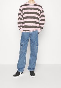 Randig långärmad skjorta i rosa och mörkgrått tyg, kombinerad med ljusblå cargobyxor med sidofickor och svarta sneakers.