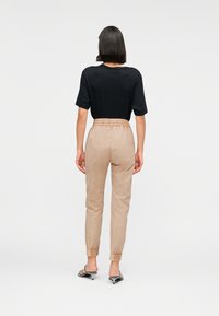 Μαύρο T-shirt με κοντά μανίκια, σε συνδυασμό με ανοιχτό μπεζ παντελόνι jogging με ελαστική μέση και ριμπ τελείωμα. Απλός σχεδιασμός.