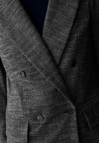 Blazer a cuadros grises con un diseño de doble botonadura, que presenta dos botones negros, solapas en pico y una tela texturizada.