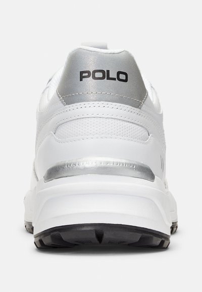 Zapatilla blanca con una parte superior de cuero suave, acento plateado en el talón, paneles texturizados y un logotipo negro de "POLO" en la parte trasera. Suela de goma.