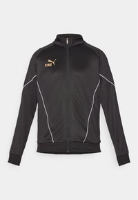 Zwarte sportsjack met witte piping accenten. Voorzien van een ritssluiting aan de voorkant, hoge kraag en gouden logo-tekst op de borst. Het materiaal is soepel en rekbaar.