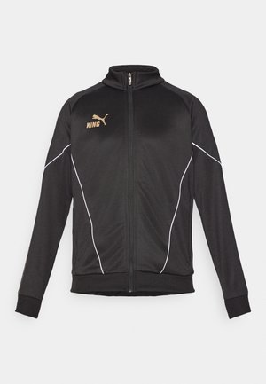 Zwarte sportsjack met witte piping accenten. Voorzien van een ritssluiting aan de voorkant, hoge kraag en gouden logo-tekst op de borst. Het materiaal is soepel en rekbaar.