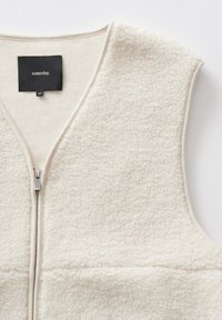 Fleece-Weste in Cremefarbe mit einer strukturierten Oberfläche. Verfügt über einen Frontreißverschluss und ein V-Ausschnitt-Design. Markenetikett mit der Aufschrift "someday" sichtbar.