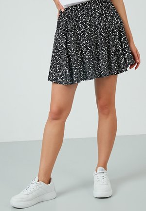 Schwarzer, ausgestellt Rock mit weißen Blumenmuster, aus leichtem Stoff gefertigt. Getragen mit weißen Sneakers, verfügt über einen gerafften Bund und Taschen.