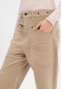 Beige corduroy pants with a relaxed fit, featuring two front pockets and two back pockets, designed with a button closure and belt loops.