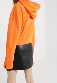 Haut court orange avec capuche, en tissu doux, associé à une mini-jupe en cuir noir. Doté de manches longues et d'une coupe décontractée.