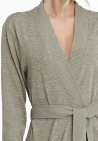 Beżowy sweter w formie szlafroka z fasonem na zapinanie, prążkowanym kołnierzem szalowym i pasującym paskiem w talii. Miękka, teksturowana tkanina.