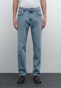 Light blue denim jeans with a straight leg, five-pocket design, visible stitching, and a conventional zipper fly. Worn with black shoes.