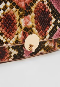 Sac à main multicolore à motif serpent avec une texture brillante, doté d'un fermoir circulaire en or et de coutures contrastées le long du bord.