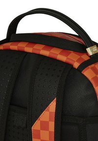 Mochila negra con acentos a cuadros naranjas, textura suave, correas de hombro acolchadas y un asa superior para facilitar el transporte.