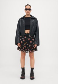Svart cropped skinnjakke over en svart crop top, kombinert med et svart miniskjørt med blomstertrykk og volangkant, samt svarte ankelstøvler.