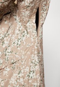 Veste de camouflage beige avec un tissu texturé et à motifs, agrémenté d'accents vert clair. Comprend des détails zippés et une coupe ample.