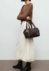 Sac à main en cuir marron à forme structurée, poignées courtes et détail zippé. Accordé avec une jupe crème et des bottes noires à lacets.