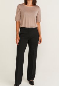 Beige T-Shirt mit kurzen Ärmeln, kombiniert mit schwarzen weit geschnittenen Hosen. Weiche Textur, entspannter Schnitt, dezenter Glanz des Oberteils und elegantes Design der Hose.