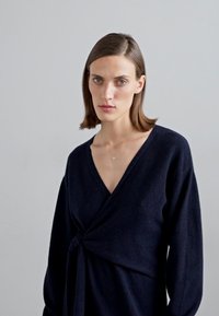 Jūras spēku sieviešu apgriezts džemperis, kas izgatavots no mīksta materiāla, ar dziļu V veida kakla izgriezumu un garām piedurknēm, kā arī mezgla detaļu jostasvietā.