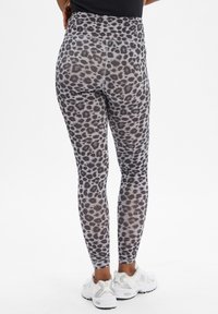 Legginsy w print w panterę z wysokim stanem, elastycznym materiałem i smukłym designem. Schemat kolorów: czarny i szary. Uzupełnione białymi butami.