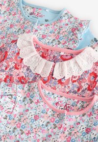 Three children's tops featuring floral patterns. Colors include light blue, pink, and purple. Textured ruffles and a lace collar detail.