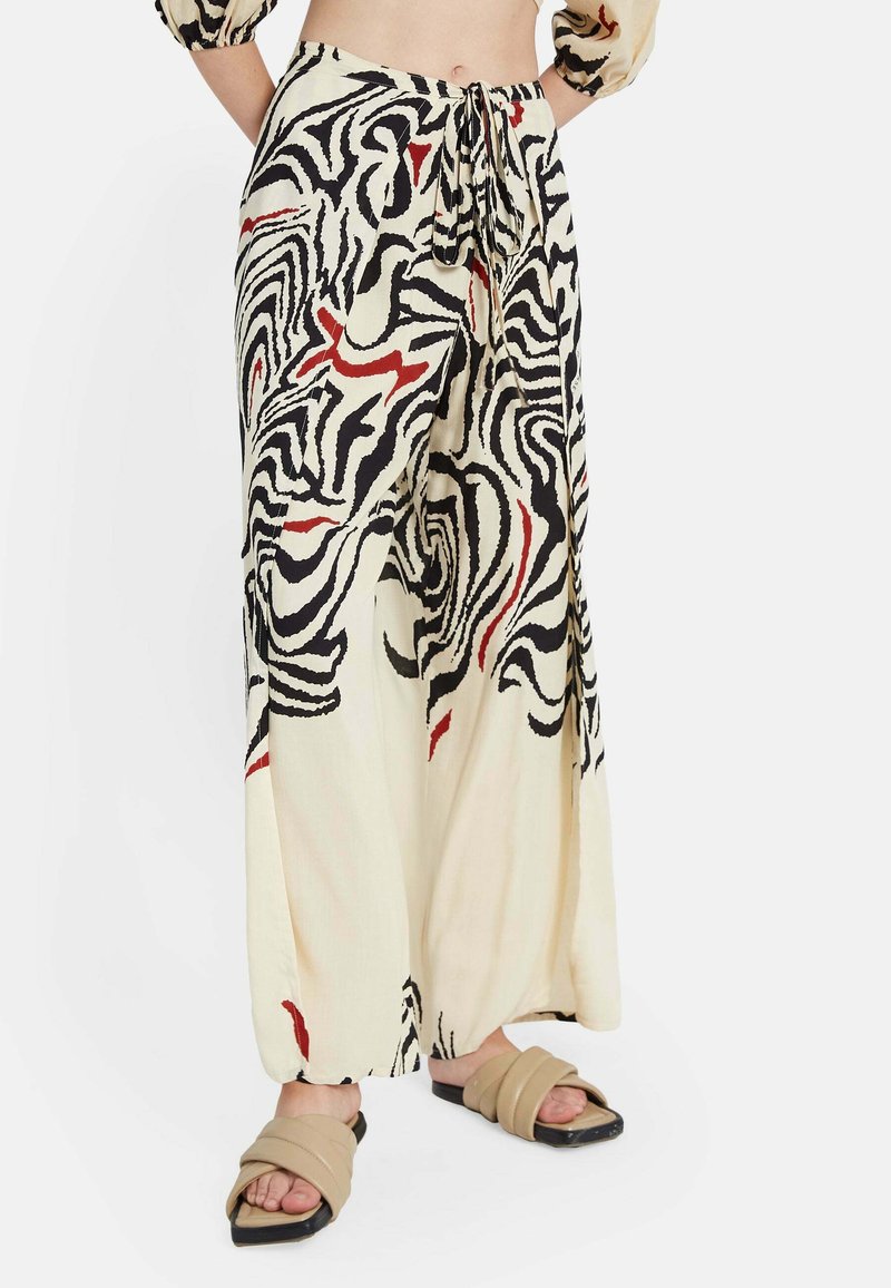 Pantalones de pierna ancha en tela color crema con un atrevido patrón abstracto en negro y rojo. Cuentan con una cintura con cordón y un diseño ligero y fluido.