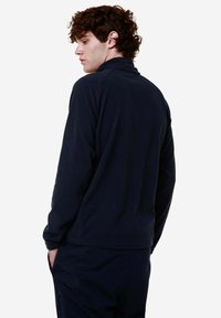 Pullover in pile blu navy con colletto alto, maniche lunghe e superficie texture. Il retro è semplice, con un design pulito e senza loghi visibili.