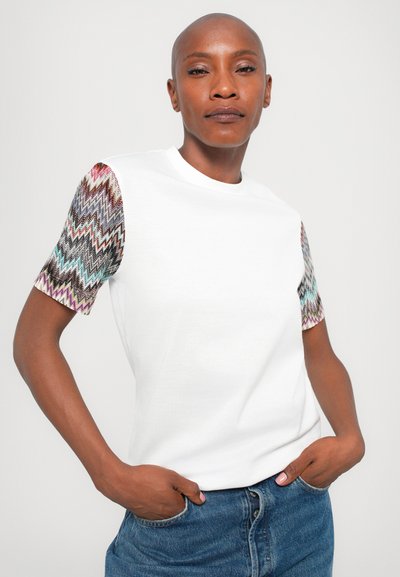 Camiseta de algodón blanca con mangas cortas en un patrón zigzagueante multicolor. Diseño casual con cuello redondo y corte holgado.