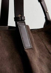 Borsa in suede marrone con manici in pelle scura, accessori in tonalità oro e una superficie texturizzata. Il design include un'etichetta in pelle prominente.