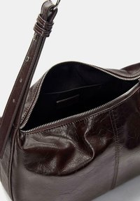 Borsa a spalla in pelle marrone con texture stropicciata, chiusura a zip e tracolla regolabile. L'interno è nero e non presenta scomparti aggiuntivi.