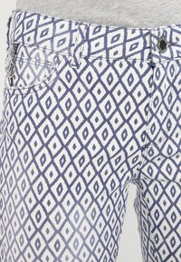 Pantalones de mezclilla blancos con un patrón de rombos azules, diseño de cinco bolsillos y una cintura clásica con cierre de botón y cremallera.