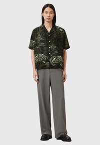 Short-sleeve black shirt with green floral patterns, paired with light gray wide-leg trousers and black shoes, standing against a white background.