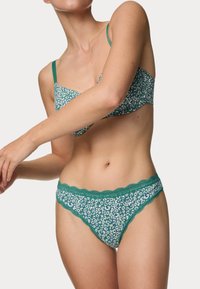 Braletka a odpovídající thong s leopardím potiskem v zelené a bílé barvě, zdobené vlnkovými krajkovými okraji a tenkými ramínky. Měkký, lehký materiál.