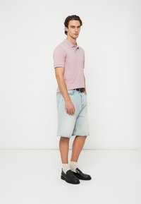 Ροζ ανοιχτό ροζ πόλο μπλουζάκι, τζιν σορτς, μαύρα slip-on παπούτσια και λευκές κάλτσες. Καθημερινό ντύσιμο με κοντά μανίκια και άνετη εφαρμογή.