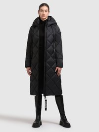 Lang sort polstret frakke med quiltet mønster, med hætte og lynlås. Båret over en sort top med høj hals og kombineret med knæhøje sorte støvler.