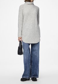 Szary dzianinowy sweter z golfem, długimi rękawami i asymetrycznym dołem, zestawiony z szerokimi niebieskimi dżinsami i małą czarną torebką.