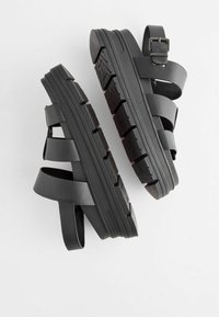 Sandales à plateforme noires avec semelles épaisses, plusieurs brides en cuir, une boucle métallique sur la bride de cheville et des semelles texturées.