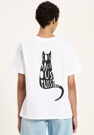 Person wearing a white T-shirt with a black cat silhouette on the back, formed by the words "COURAGEOUS PUSS" in bold letters.