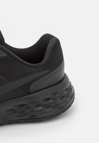 Close-up di una scarpa sportiva nera, con una tomaia in rete testurizzata, colletto imbottito e suola ammortizzata con battistrada a motivo.