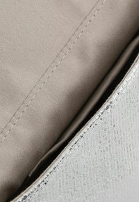 Ezüst, texturált anyag fényes felülettel, bézs színű bélés anyagot és a szélén látható varrásokat felfedve.