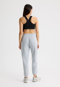 Sujetador deportivo negro con tirantes anchos, combinado con pantalones de chándal grises claros que presentan una cintura elástica y tobillos ajustados. Zapatillas plateadas visibles.