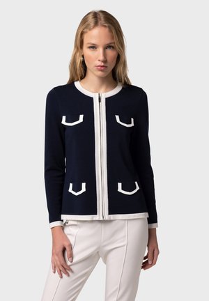 Laivaston cardigan, jossa on valkoisia yksityiskohtia, vetoketj closure ja neljä taskua. Ominaisuuksiin kuuluu pyöreä kaula-aukko ja pitkät hihat; valmistettu teksturoidusta neuloksesta.