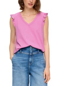 Różowa kamizelka na karku z falbaniastymi rękawami, wykonana z miękkiego materiału. Zestawiona z niebieskimi dżinsami o wysokim stanie.