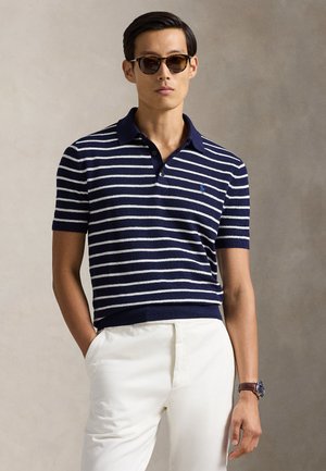 Granatowo-biała koszulka polo w paski z krótkim rękawem, kołnierzykiem, prążkowanym wykończeniem i małym niebieskim logo na piersi. W zestawie z białymi spodniami.