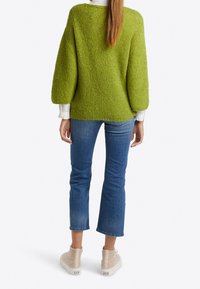 Groen gebreide trui met textuur, losse pasvorm en ballonmouwen, gecombineerd met cropped blauwe spijkerbroek en lichtgekleurde hoge sneakers.