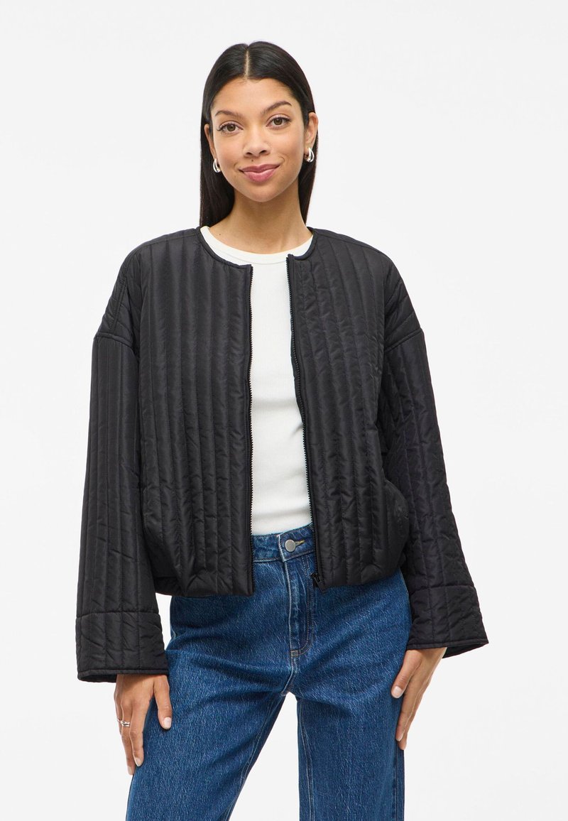 Juodas siuvinėtas švarkas su apvalia apykakle, priekiniais užtrauktukais ir plačiomis rankovėmis. Dėvimas ant balto marškinėlio, derinamas su mėlynomis aukštu juosmeniu džinsais.