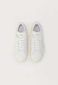 Hvide lædersneakers med teksturerede detaljer, flade snørebånd, perforerede elementer og en gummifarvet gummisål. Bemærkelsesværdigt brandlogo på tungen.