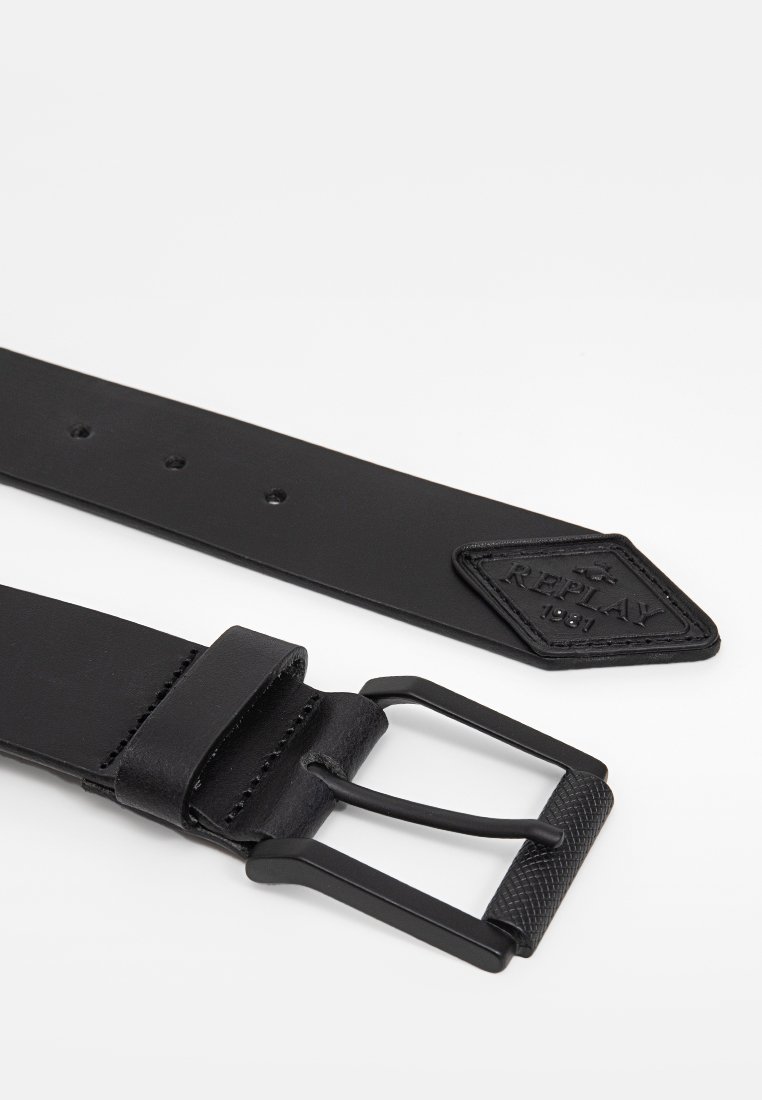 Ceinture en cuir noir avec une boucle noire texturée et un patch logo en forme de diamant. Comprend plusieurs crans pour un ajustement.