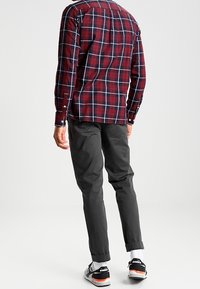 Rood en marineblauw geblokt overhemd met lange mouwen en knopenmanchetten, gecombineerd met grijze broeken en zwarte sneakers met oranje accenten.