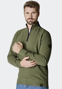 Zielony, prążkowany sweter z wysokim kołnierzem, czarnym zamkiem błyskawicznym i czarną naszywką na lewym rękawie. Posiada żółte wykończenie wzdłuż ramienia.